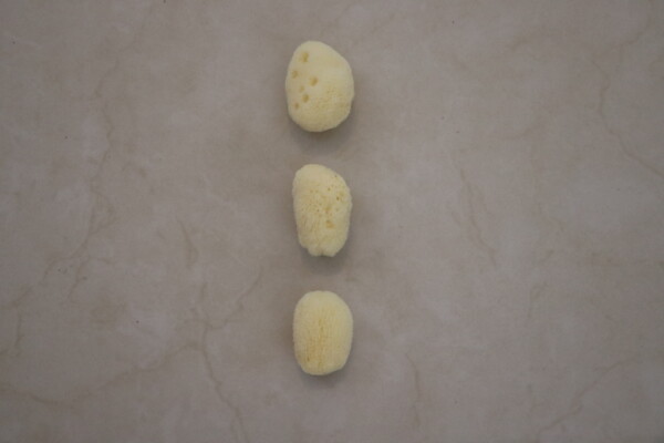 Natural sea sponge trio displayed on a smooth gray marble surface showcasing their texture and unique shapes perfect for spa treatments and gentle exfoliation